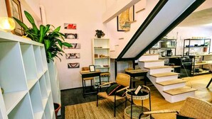 A modern living space with a staircase leading to an upper level, a bookshelf, and a seating area with a woven rug.
