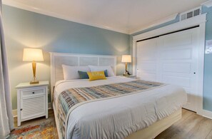 A bedroom with a bed, two bedside tables with lamps, a white door, and a patterned rug. - Experience oceanfront comfort at 0304 Bountiful Bliss in Carolina Beach! (Carolina Beach)