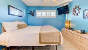 Un dormitorio con cama, ventilador de techo, televisor y ventana con persianas.