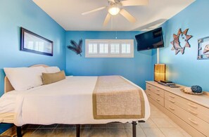 Une chambre à coucher avec un lit, un ventilateur de plafond, une télévision et une fenêtre avec des stores.