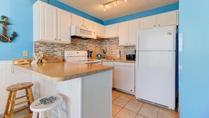 Una cocina con armarios blancos, salpicadero de azulejos, una isla central con taburetes y un refrigerador.