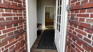 A hallway with a brick wall, a white door, and a dark mat at the entrance. - Vacation home Alte Schule (Dornumersiel)