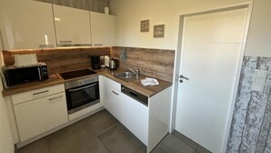 A compact kitchen with a microwave, oven, sink, and wooden countertop. - Vacation home Alte Schule (Dornumersiel)