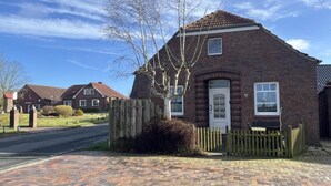A brick house with a white door, a small porch, and a wooden fence. - Vacation home Alte Schule (Dornumersiel)