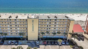 Ein mehrgeschossiges Hotel mit zentralem Eingang, Parkplatz und Blick auf den Strand.