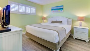 Quarto com cama, duas mesas de cabeceira, um criado-mudo, televisão e janela com persianas.
