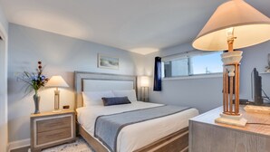 A bedroom with a bed, bedside tables, a lamp, a window with curtains, and a painting on the wall. - Oceanfront 1-bedroom retreat in Carolina Beach 307 (Carolina Beach)