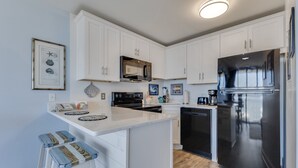 A kitchen with white cabinets, a stainless steel refrigerator, and a wooden floor. - Oceanfront 1-bedroom retreat in Carolina Beach 307 (Carolina Beach)