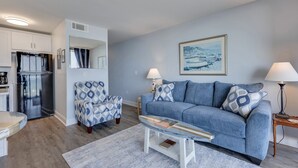 A modern living room with a sofa, armchair, coffee table, and a painting on the wall. - Oceanfront 1-bedroom retreat in Carolina Beach 307 (Carolina Beach)