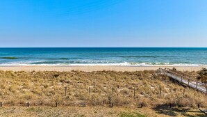 A beach with a wooden boardwalk leading to the ocean, sandy dunes, and a clear blue sky. - Oceanfront 1-bedroom retreat in Carolina Beach 307 (Carolina Beach)