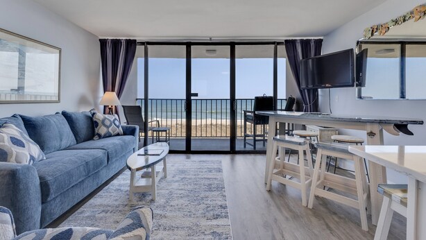 A room with a sofa, coffee table, TV, and a balcony with a view. - Oceanfront 1-bedroom retreat in Carolina Beach 307 (Carolina Beach)
