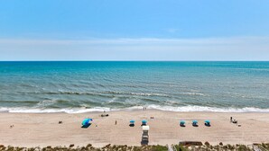 Ein Strand mit blauem Himmel, ruhiger See und mehreren Sonnenschirmen.