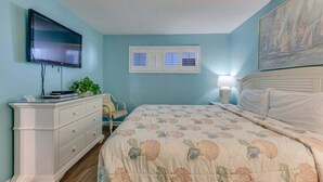 Ein Schlafzimmer mit Bett, Kommode, Fernseher, Fenster und Kunstwerken.