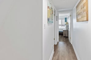 A hallway with white walls, wooden flooring, and a door leading to a bedroom. - Pinnacle Port with Gulf & Lake Views | Pools | West End PCB (Panama City Beach)