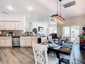 A modern kitchen with a central island, white cabinetry, and a dining area with a wooden table and chairs. - E511JA - Our Happy Place 3B/2bath - Pool & Arcade (Davenport)