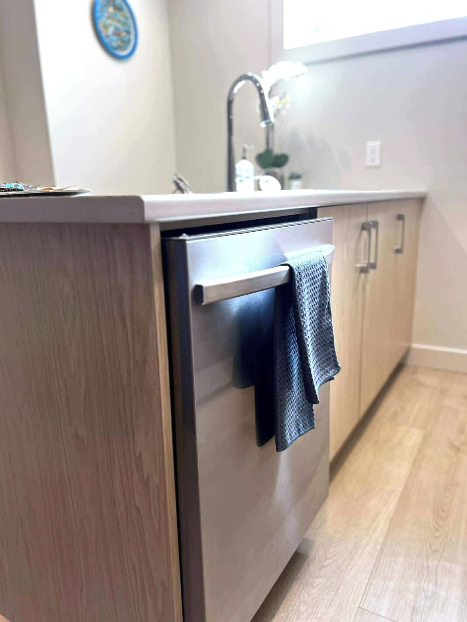 A compact kitchen with a built-in dishwasher, wooden cabinets, and a window providing natural light.