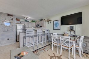 A compact kitchen with a dining area, a flat-screen TV, and a ship wheel decoration. - 0312 Captains Quarters: Stunning 2-bedroom oceanfront condo in Carolina Beach. (Carolina Beach)