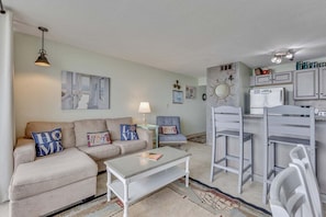 A living room with a sofa, coffee table, and a dining area with a chair and a small table. - 0312 Captains Quarters: Stunning 2-bedroom oceanfront condo in Carolina Beach. (Carolina Beach)