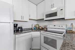 A kitchen with white cabinets, a microwave, a stove, and a dishwasher. - Experience beachfront bliss in this cozy 1-bedroom, Carolina Beach retreat. (Carolina Beach)