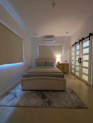 A bedroom with a bed, bedside lamp, nightstand, and a sliding door. - Modern 3 BR- 3 bath, Cascade, 5 mins from Downtown POS, Pool (Port of Spain)