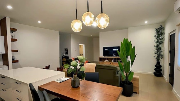 Una cocina moderna con una isla central, iluminación colgante y un comedor con sillas.