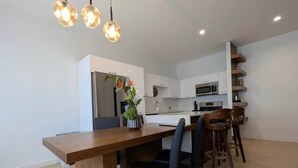 Una cocina moderna con armarios blancos, una mesa de comedor de madera y lámparas colgantes.