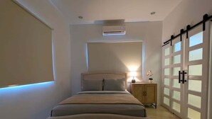 A bedroom with a bed, bedside lamp, nightstand, and a sliding door. - Modern 2 BR | Pool | 5 mins from Downtown POS (Port of Spain)