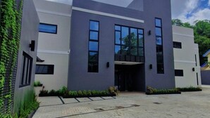 A modern building with a flat roof, large windows, and a paved entrance area. - Modern 2 BR | Pool | 5 mins from Downtown POS (Port of Spain)