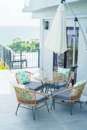 Ein Balkon mit Korbstühlen, einem Glastisch, einem weißen Sonnenschirm und Blick aufs Meer.