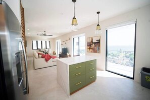 Eine moderne Küche mit einer grünen Kochinsel, ein Essbereich mit einem weißen Sofa und ein großes Fenster mit Blick auf die Stadt.