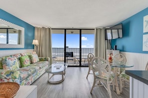 Ein Zimmer mit einer Couch, einem Glastisch, einem Sessel und Blick auf den Strand.