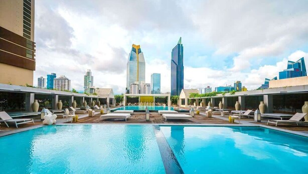 Una piscina en la azotea con sillones de descanso, vista a modernos rascacielos y cielo despejado.
