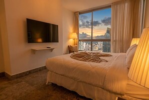 Een hotelkamer met een groot bed, een flatscreen televisie aan de muur, een raam met uitzicht op de stad en een lamp op het nachtkastje.