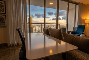 Une chambre d’hôtel dotée d’une grande fenêtre donnant sur la ville, d’une table à manger, d’un canapé et d’un fauteuil bleu.