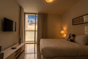 Ein Hotelzimmer mit einem Bett, einem Fernseher, einer Lampe, einem Nachttisch und Blick zum Himmel durch das Fenster.