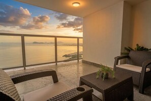 Ein Balkon mit Korbmöbeln, einem Blumentopf und Blick auf das Meer und eine Brücke.