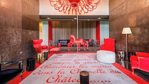 A lobby with a red and white carpet, a chandelier, red chairs, a white sofa, and a red horse statue. - 31J Apto en Yoo, Lujoso con Vista al Mar de 2 rec (Panamá)