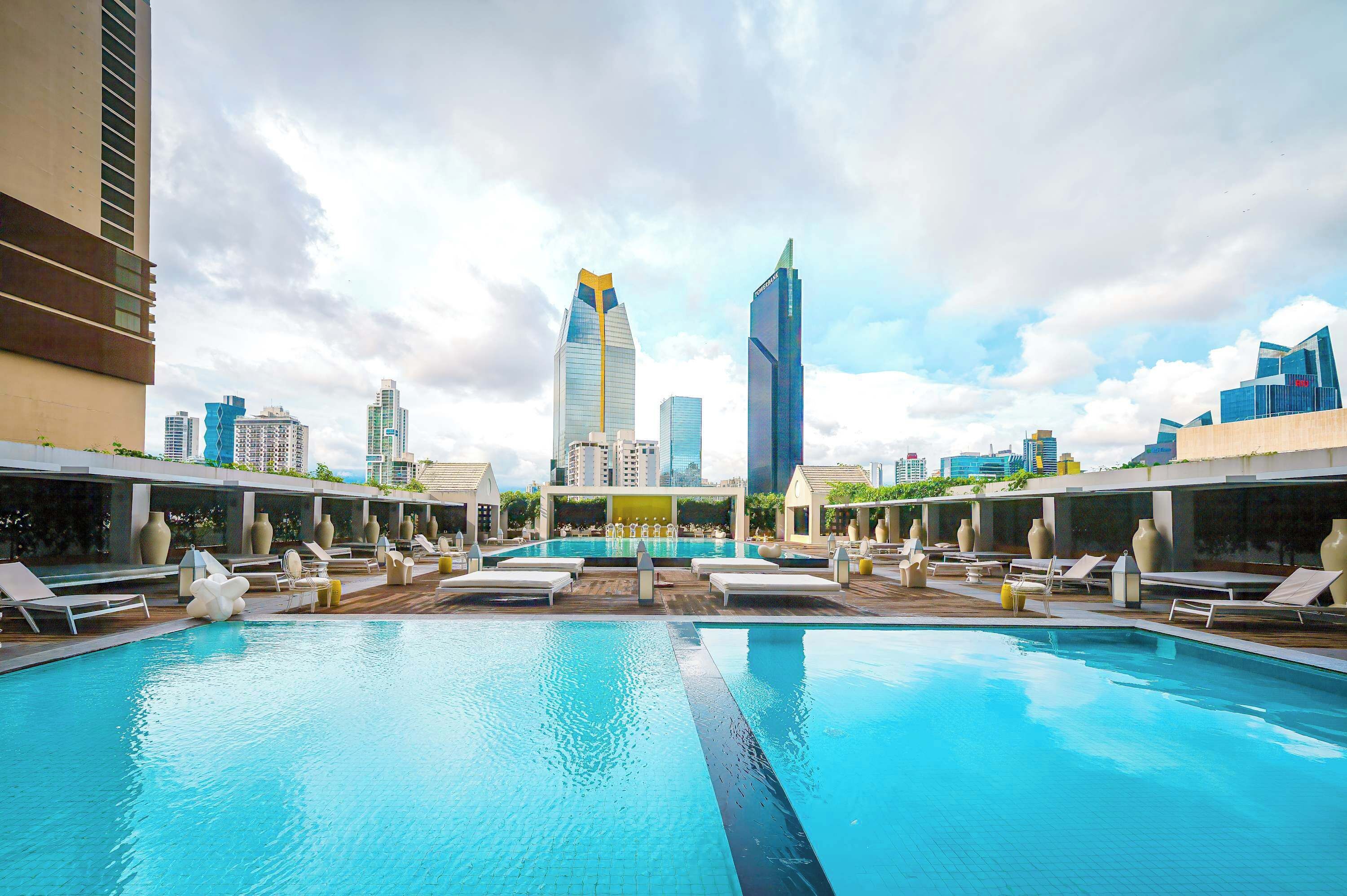 A rooftop pool with lounge chairs and a city skyline in the background.
