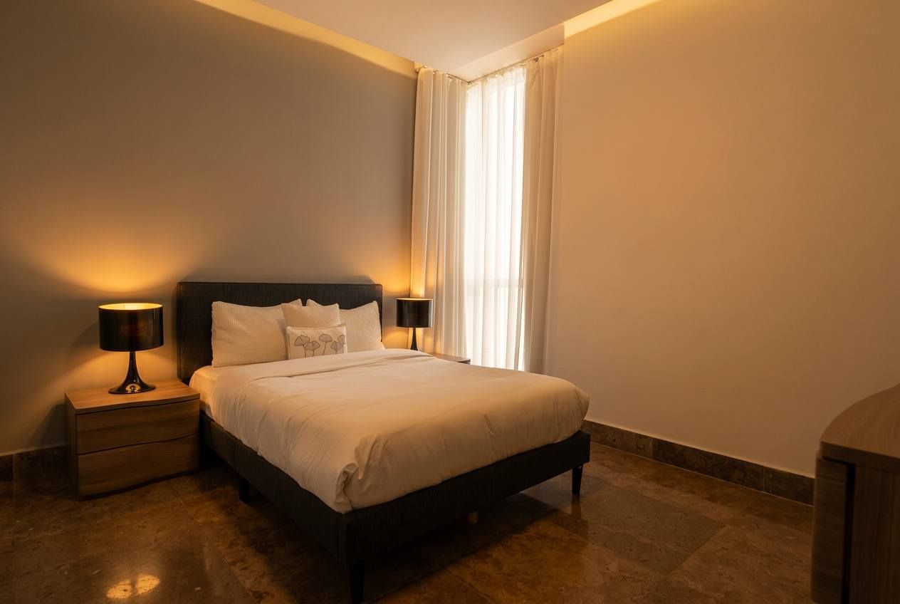 Una habitación de hotel con cama, mesitas de noche y ventana con cortinas.