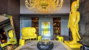A lobby with a chandelier, a yellow sofa, a black ottoman, and a statue. - 31J Apto en Yoo, Lujoso con Vista al Mar de 2 rec (Panamá)