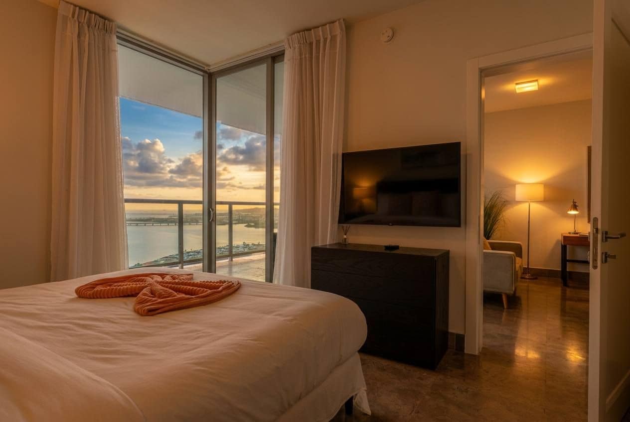 Une chambre d’hôtel avec un lit, un téléviseur à écran plat, un bureau et une vue sur la mer.