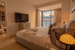 A hotel room with a large bed, a television, a balcony with a view of the sea, and a lamp. - Apto 48C con vista al mar y con 1 dormitorio (Panamá)
