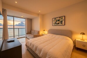 A hotel room with a large bed, a desk, a chair, a nightstand, a lamp, a painting, and a view of the sea. - Apto 48C con vista al mar y con 1 dormitorio (Panamá)