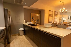 A modern kitchen with a large island, stainless steel appliances, and a dining area with a chandelier. - 32B Apto en Yoo con Vista al mar en Avenida Balboa (Panamá)