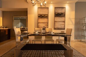 A modern dining area with a glass table, white chairs, and a chandelier. - 32B Apto en Yoo con Vista al mar en Avenida Balboa (Panamá)