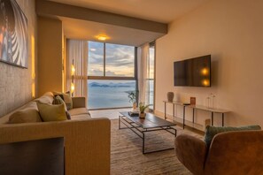 En moderne stue med sofa, sofabord og fjernsyn, store vinduer med havudsigt og minimalistisk indretning.