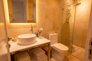 Et badeværelse med en rund vask, toilet, brusekabine i glas og et spejl over vasken.