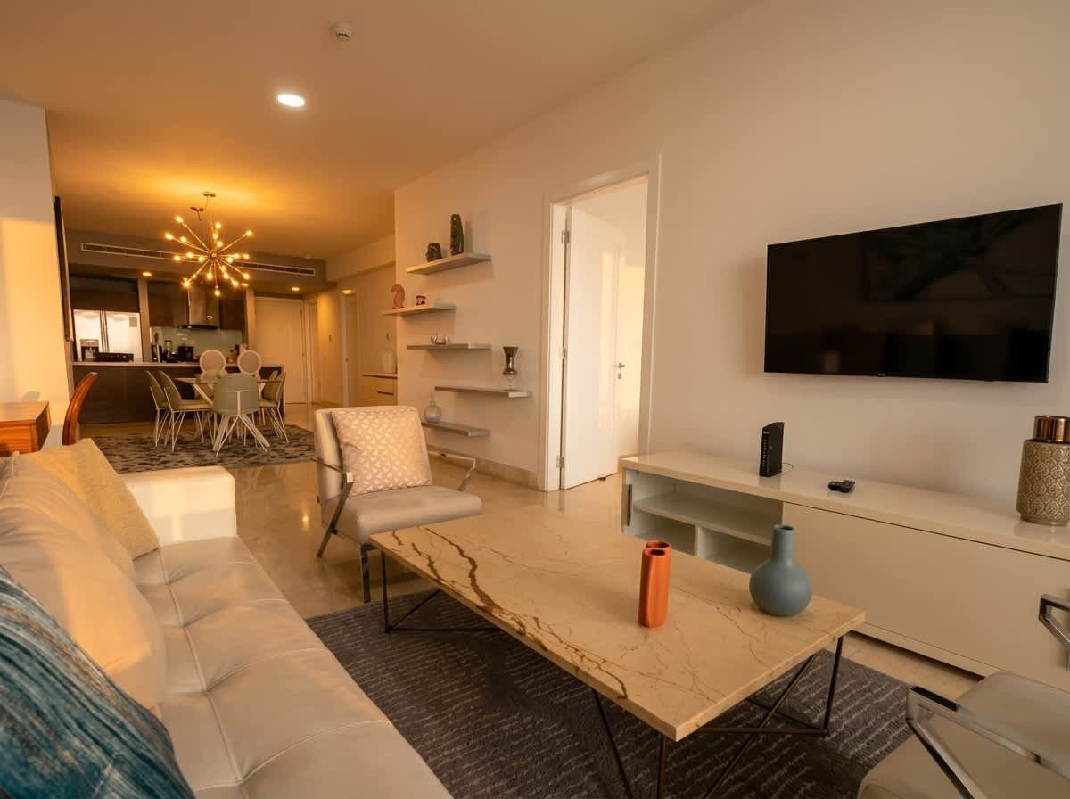 Ett modernt vardagsrum med en soffa, ett soffbord och en tv. I bakgrunden syns ett kök.