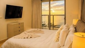 A hotel room with a bed, a TV, a window with curtains, and a view of the sea. - Lujoso Apto 34A, vista al mar con dos recamaras (Panamá)