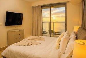 A hotel room with a bed, a TV, a window with curtains, and a view of the sea. - Lujoso Apto 34A, vista al mar con dos recamaras (Panamá)